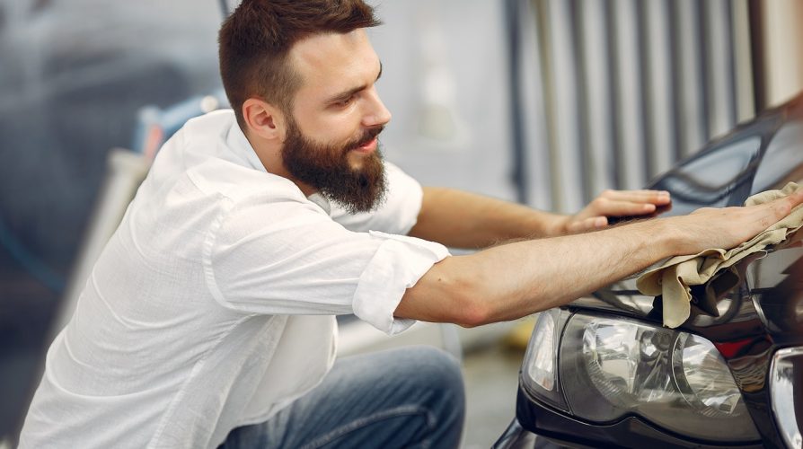 Man in a white shirt. Worker wipes a car. Male holding a rag in his hand
